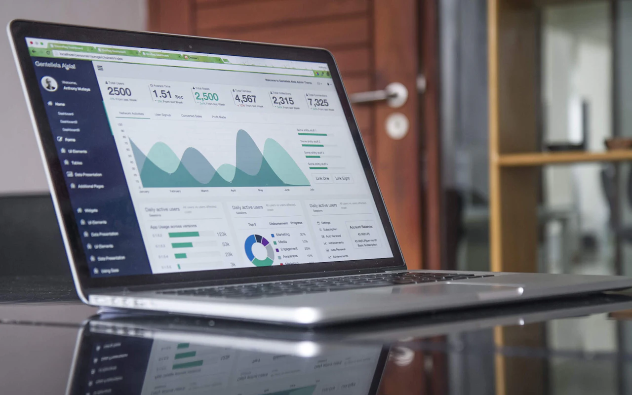 A laptop on a polished table showing a dashboard of charts and figures.