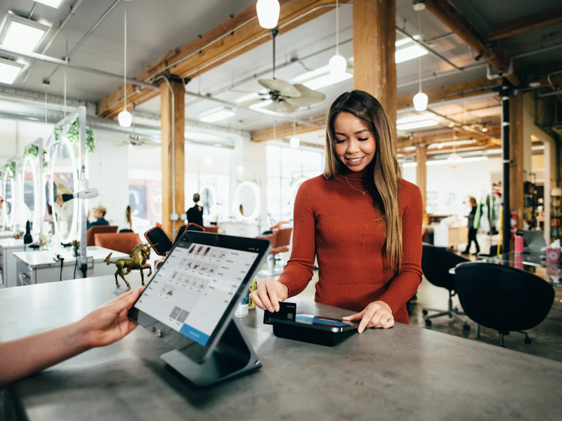 A shop assistant taking a card payment at a counter tablet.
