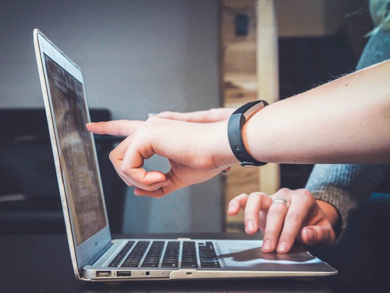 A hand pointing at something on a laptop screen while another hand rests on the keyboard.
