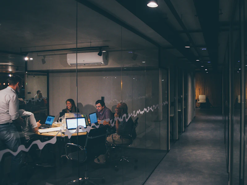 A lit meeting room seen through glass in an otherwise dark office at night.